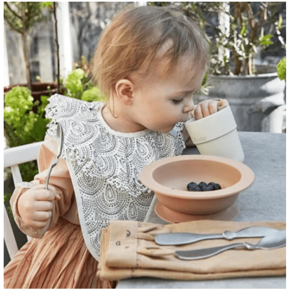 A baby wearing her bib and eating blueberries detailing how easy it is to clean the bibs due to the material used