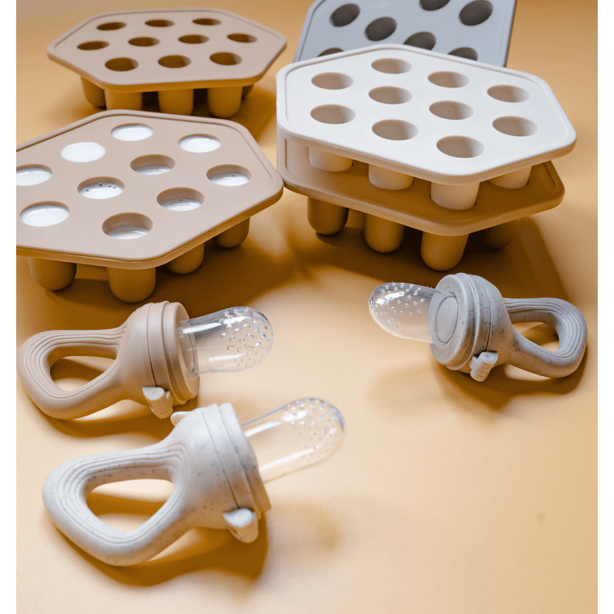 A silicone breast milk and baby food freezer tray with matching feeders, designed for preparing popsicles. The image shows multiple trays with rounded compartments and attached feeding devices with a soft tip.