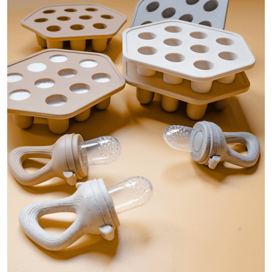 A silicone breast milk and baby food freezer tray with matching feeders, designed for preparing popsicles. The image shows multiple trays with rounded compartments and attached feeding devices with a soft tip.