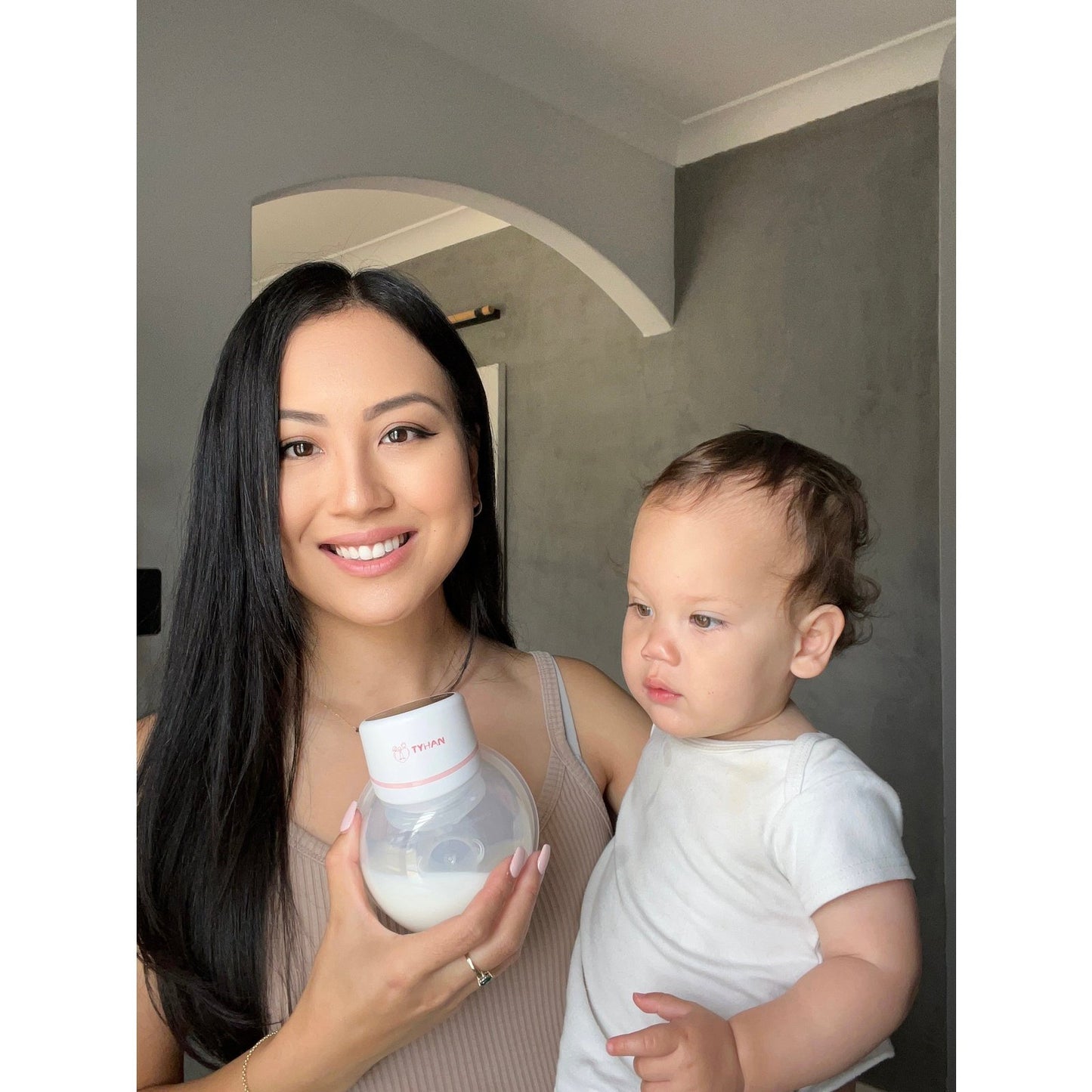 Mum holding her baby and her wearable breast pump showing the milk she collected after using her breast pump